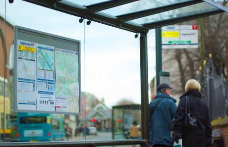 An image of a bus shelter with the bus timetable visible whilst a couple walk away in the distance