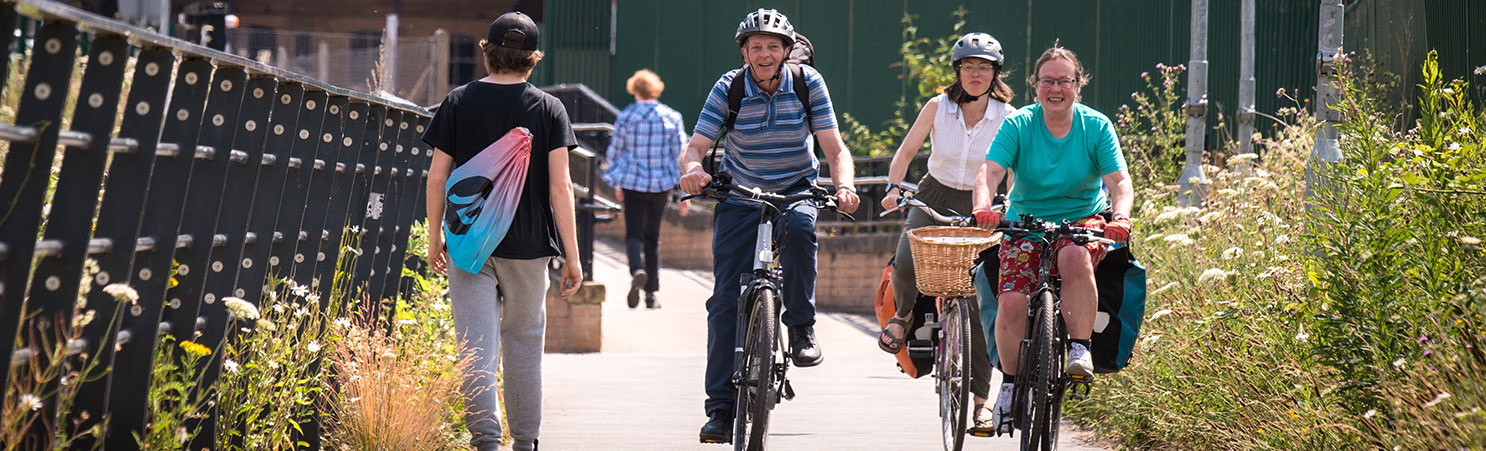 Three cyclists are smiling as they ride on a cycle path.
